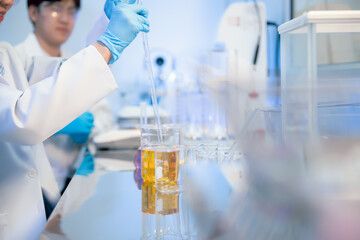 Fototapeta premium Pharmaceutical research, close up scientist hands in blue gloves using pipette with glass dropper in laboratory. Transferring liquid for vaccine or medicine discovery research.