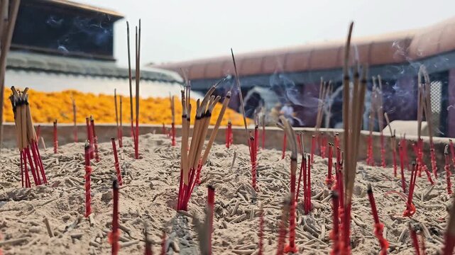 Burning incense sticks placed in ash at outdoor temple altar with rising smoke. Close up footage of aromatic joss sticks used for prayer ritual and spiritual offering in Asian religious culture. Macro