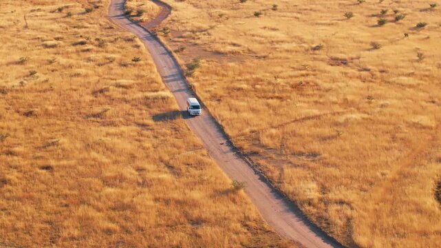 Aerial footage of white van traveling along winding dirt road through golden savanna grasslands in Sierra Madre Occidental mountains near Durango, Mexico during warm sunset light.