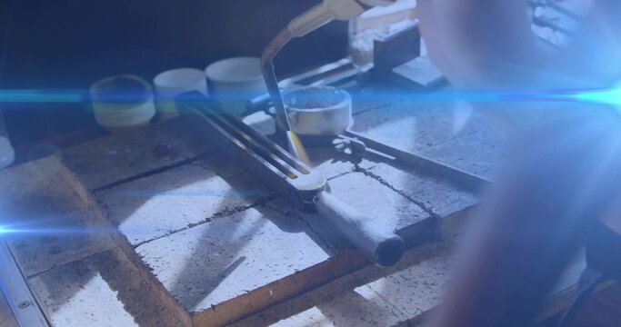Heating small crucible with tongs over firebrick at jewelry bench, with gloved hand and torch flame