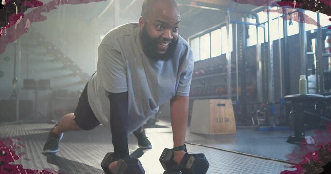 Performing plank-style push-up, adult man wearing layered athletic wear using hex dumbbells at gym