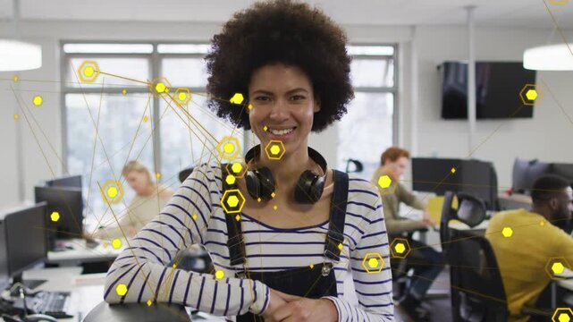 Woman leaning at desk in biz, yellow hex overlay rising, camera pushing, smiling showing teamwork