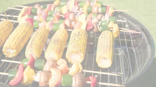 Glowing charcoal heating kettle grill, corn charring and vegetable skewers softening for serving