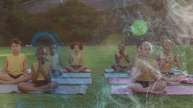 Eight kids meditating on grass, following cue and pressing palms with particles obscuring kids