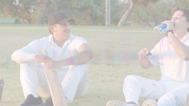 Right cricketer unsealing blue bottle and drinking, left cricketer shifting bat preparing return