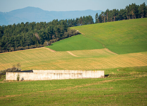 Rolling agricultural fields with concrete manure storage facility in rural Slovakia. Contrast between nature and farming infrastructure in spring countryside landscape.