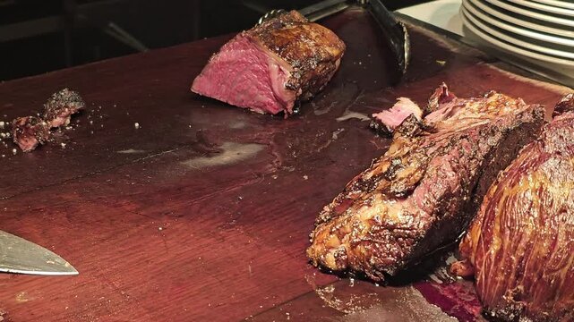 Roasted beef cuts and sliced medium rare steak on wooden carving board with meat juices and crispy smoked crust in steakhouse serving station. Barbecue buffet and grilled meat preparation concept