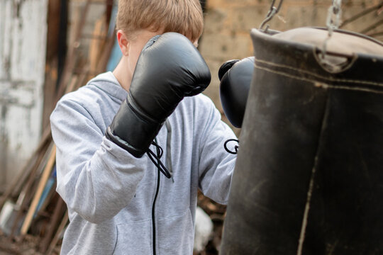 Teenage Boy Training with a Punching Bag Outdoors Wearing Black Boxing Gloves and Grey Hoodie