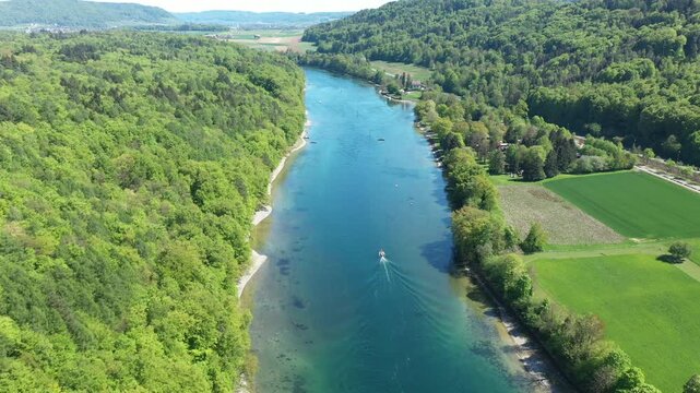 Drone flying ahead of motorboat on river with wide panoramic landscape, aerial countryside view