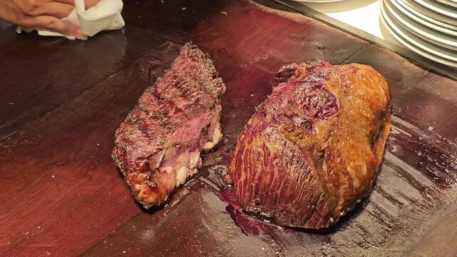 Roasted beef cuts resting on wooden carving board at restaurant kitchen counter. Cooked meat with grilled crust and visible juice prepared for steak serving and barbecue cuisine concept