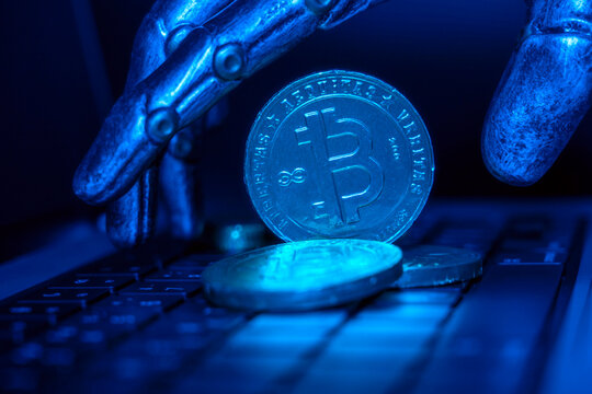 Robotic hand rests on keyboard. Blue light illuminates cryptocurrency coins. Metallic fingers touch digital currency tokens. Symbolizes blockchain technology and AI investment