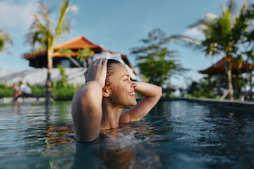 Fototapeta premium A poolside scene shows a woman in clear water, enjoying relaxation and vacation vibes at a resort, with summer sunlight, a carefree smile, and happiness radiating as she lounges and swims.