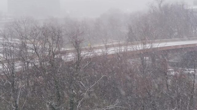 View of heavy snowfall over a highway bridge and bare trees with a car driving through the winter storm in Tysons, Virginia, United States.