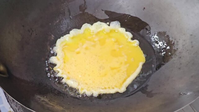 Stir frying squid rings and tentacles with egg in hot wok close up, seafood and omelet cooking process in Asian kitchen with oil sizzling and spatula mixing ingredients over high heat