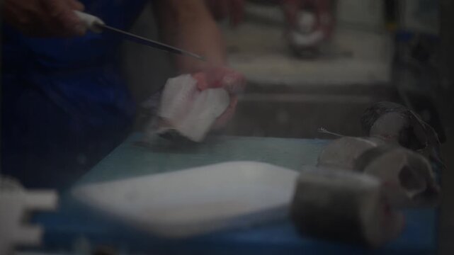 View of a fishmonger's hands skillfully filleting fresh fish on a blue cutting board at Mercado da Vila Cascais, Lisboa, Portugal.
