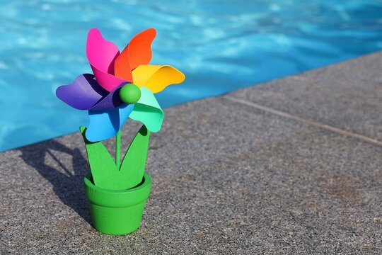 
Colorful windmill in the shape of a potted flower with a swimming pool in the background. Garden decoration.