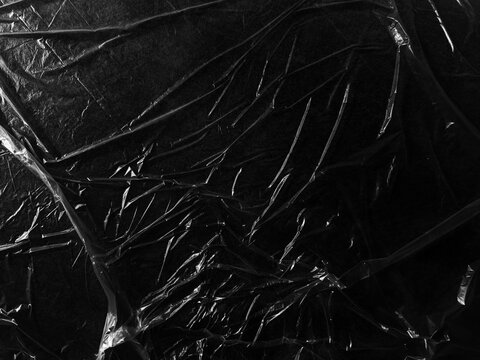 Wrinkled plastic wrap texture on a black background. Cellophane package wallpaper
