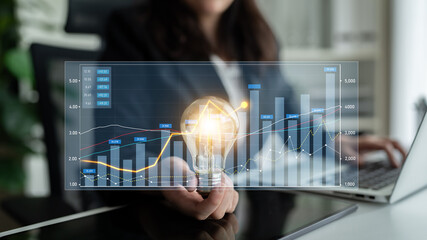 Business professional presents an innovative idea using a light bulb and financial graphs, symbolizing growth and creativity in a modern office environment. Scalp © InfiniteFlow