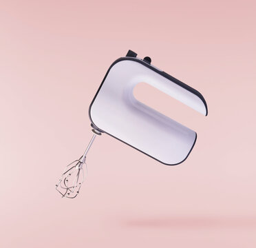 Levitating electric hand mixer with metal beaters isolated on a pink background. Minimalist zero gravity studio kitchen appliance concept.