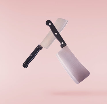 Levitating crossed heavy meat cleaver knife with black handles isolated on a pink background. Creative zero gravity concept.