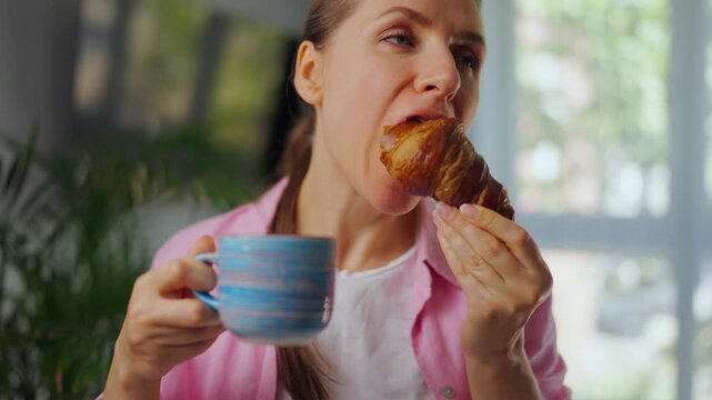 Woman enjoying a fresh croissant and coffee for breakfast. Slow motion