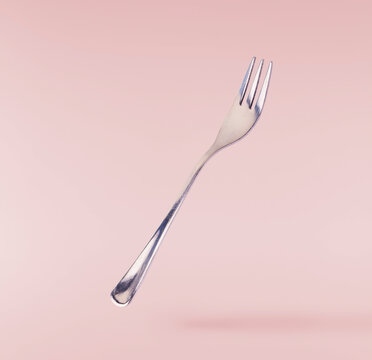 Levitating metal fork  isolated on a pink background. Minimalist zero gravity tableware concept.
