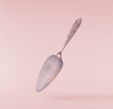 Levitating vintage silver cake server spatula isolated on a pastel pink background. Minimalist zero gravity studio tableware photography concept.
