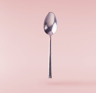 Levitating metal spoon isolated on a pink background. Minimalist zero gravity tableware concept.