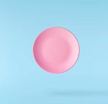 Levitating empty ceramic plate isolated on a pastel blue background. Minimalist zero gravity studio tableware photography concept.