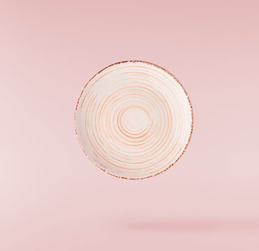 Levitating empty ceramic plate isolated on a pink background. Minimalist zero gravity studio tableware photography concept.