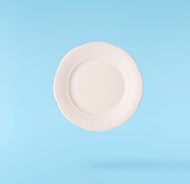Levitating empty ceramic plate isolated on a pastel blue background. Minimalist zero gravity studio tableware photography concept.