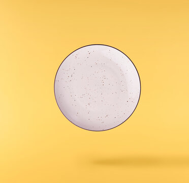 Levitating empty ceramic plate isolated on a yellow background. Minimalist zero gravity studio tableware photography concept.