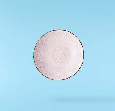 Levitating empty ceramic plate isolated on a pastel blue background. Minimalist zero gravity studio tableware photography concept.