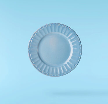 Levitating empty ceramic plate isolated on a pastel blue background. Minimalist zero gravity studio tableware photography concept.