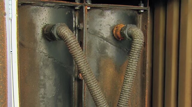 Close view of a robust air filter apparatus with corrugated conduits and rusted metal panels.