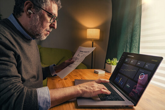Senior man analyzing financial data on laptop with digital dashboard at home