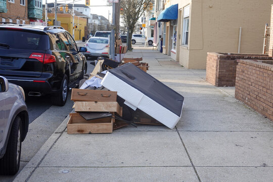 Old mattress and broken wooden furniture on the sidewalk near the curb waiting for trash pickup