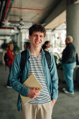Fototapeta premium Young male student holding book, smiling at university campus, representing education, youth, and learning