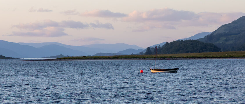 A small sailboat sits silently waiting on a buoy in a Scottish loch on a windy day, waiting to be used.