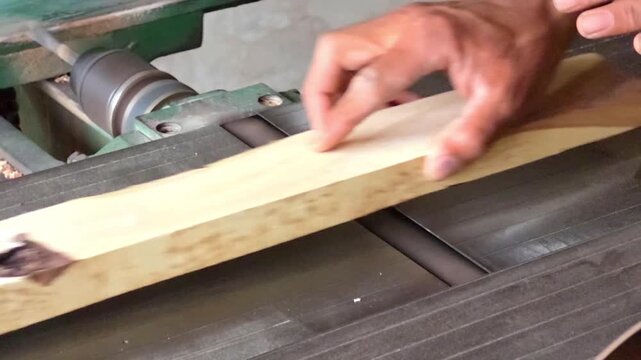Woodworker flattening a raw timber plank using a professional jointer machine in a bright workshop environment High Quality Footage