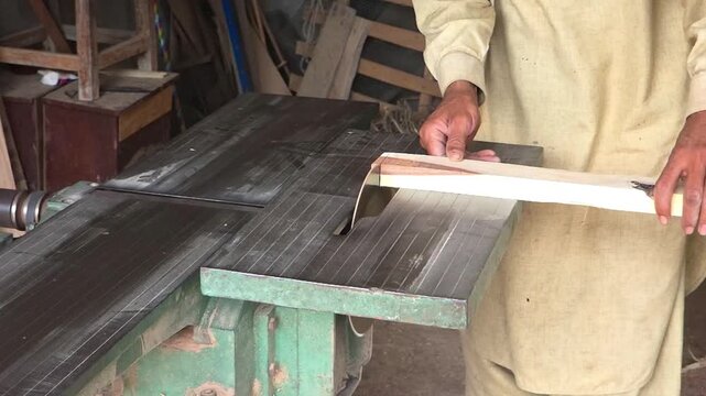 Woodworker precisely cutting a light timber plank on an industrial table saw inside a traditional workshop environment High Quality Footage