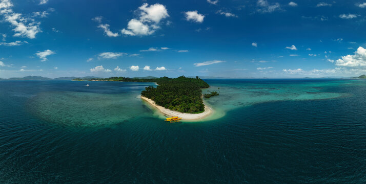 A breathtaking aerial view of a tropical Maxma Island surrounded by crystal-clear turquoise waters, with a narrow sandbar curving along its edge.
