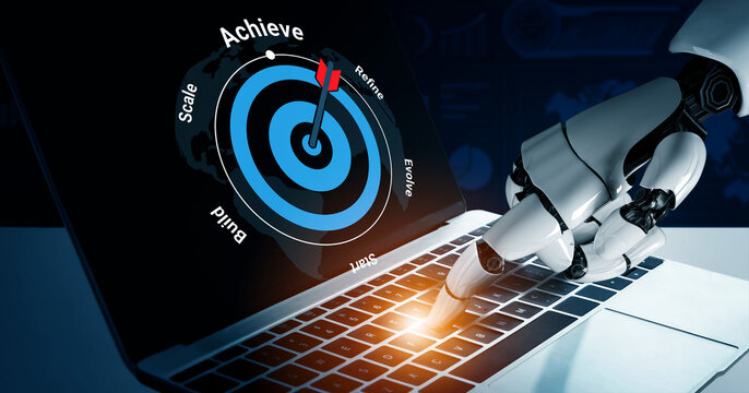 A robotic hand interacts with a laptop keyboard while a goal-setting graphic is displayed on the screen, symbolizing the future of technology and innovation. Gantry