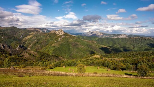 View of rolling green hills and haystacks in a rural landscape under a blue sky in Salciua de Jos, Alba County, Romania.
