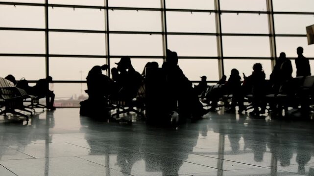 Silhouettes of unrecognizable people in airport waiting room against background of window 