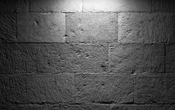 A close-up view of a rough gray stone wall illuminated from above, revealing gritty textures and grayscale tones. Great for architectural, interior, or backdrop visuals with a vintage, industrial feel