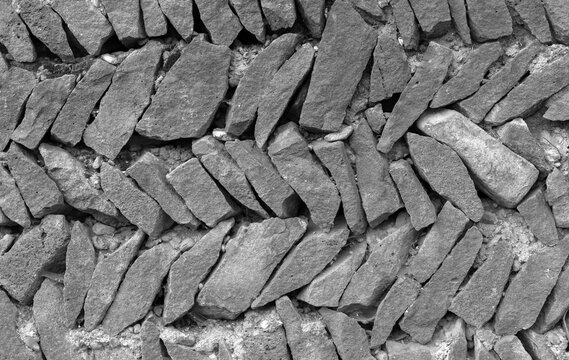 Close-up of a stacked, dry-stone wall built from irregular black rocks. The rugged texture and orderly arrangement convey strength and rustic charm, ideal for architecture, landscaping, or outdoor