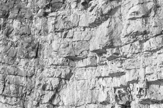 A close-up view of a rugged gray cliff wall showing layered stones and weathered texture. Ideal for nature, geology, outdoor and landscape projects