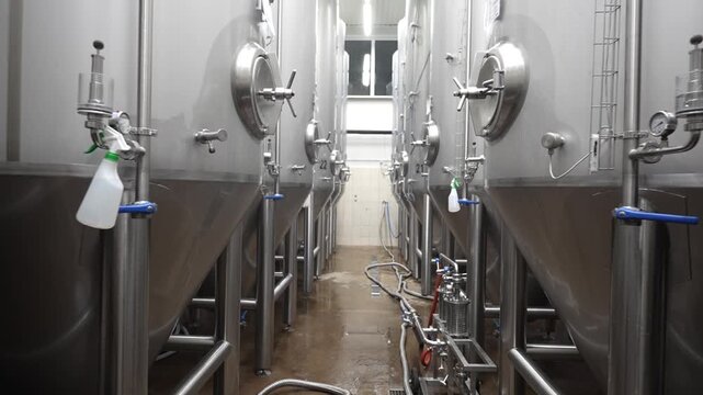 Brewery interior showcasing stainless steel fermentation tanks in a clean, well-lit environment with visible piping and numbered tanks