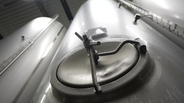 Stainless steel fermentation tanks in a brewery, showcasing the progression of brewing equipment and condensation on surfaces